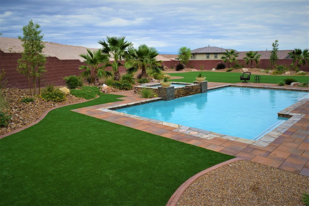 A pool with grass and palm trees in the background.