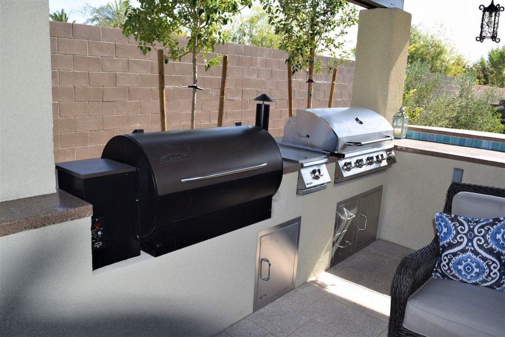 A grill and smoker on the patio of an outdoor kitchen.