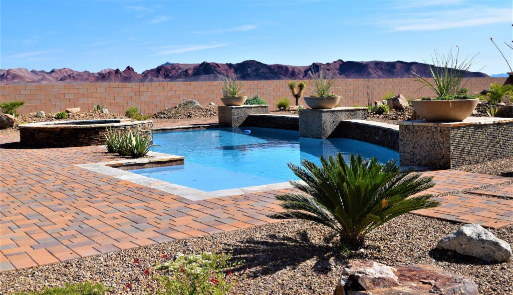 A pool with a brick patio and a desert landscape.