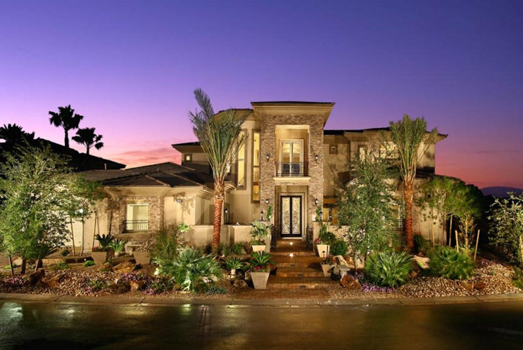 A large home with palm trees and lights in the evening.